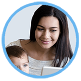 Smiling young woman holds a child while paying a medical bill on a tablet computer.