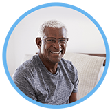 Happy senior citizen man wearing glasses smiles while sitting on a couch.